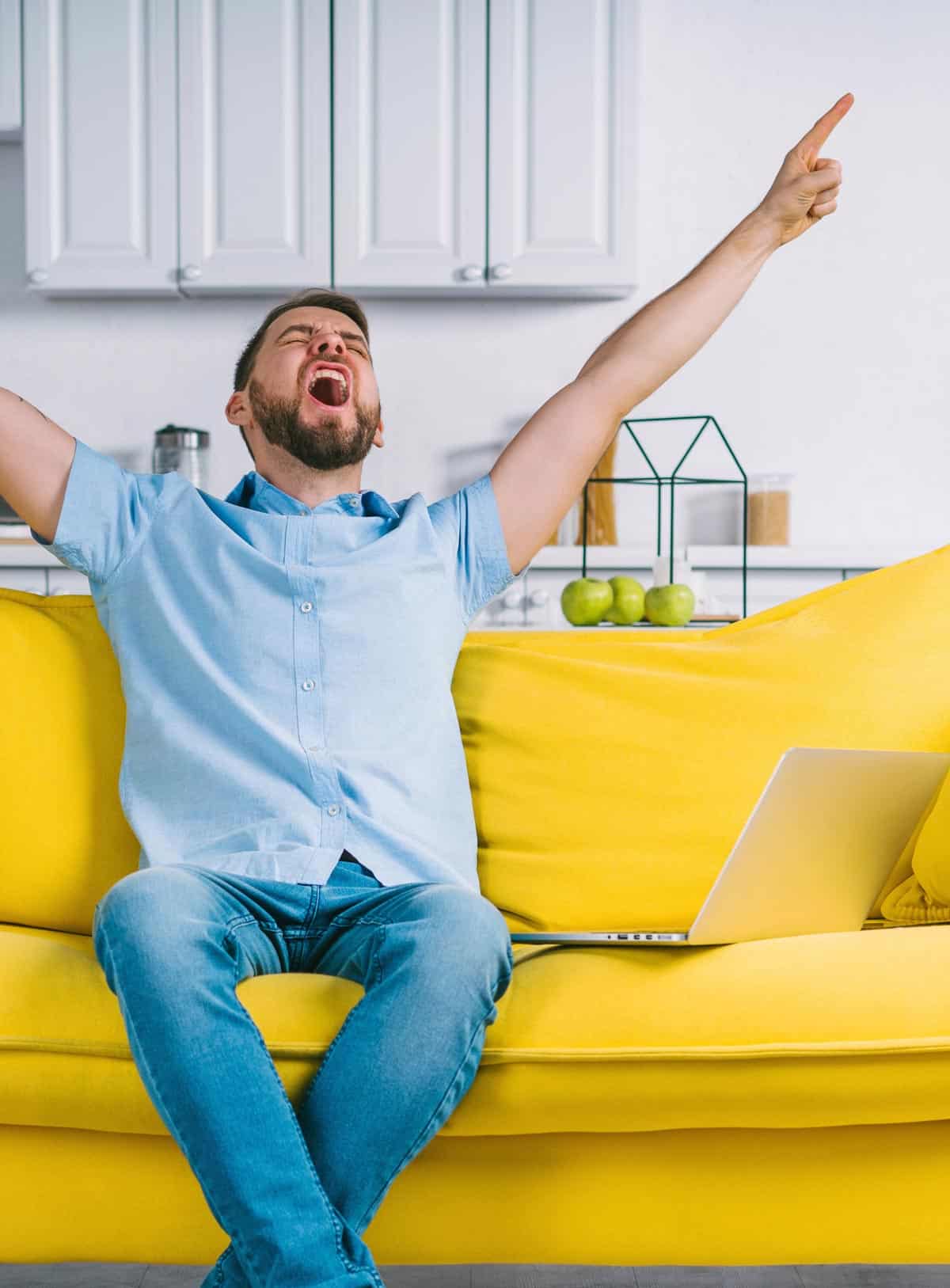 LuckyHome Baudienstleistungen - junger Mann sitzt auf einem gelben Sofa und freut sich, dass er LuckyHome gewählt hat